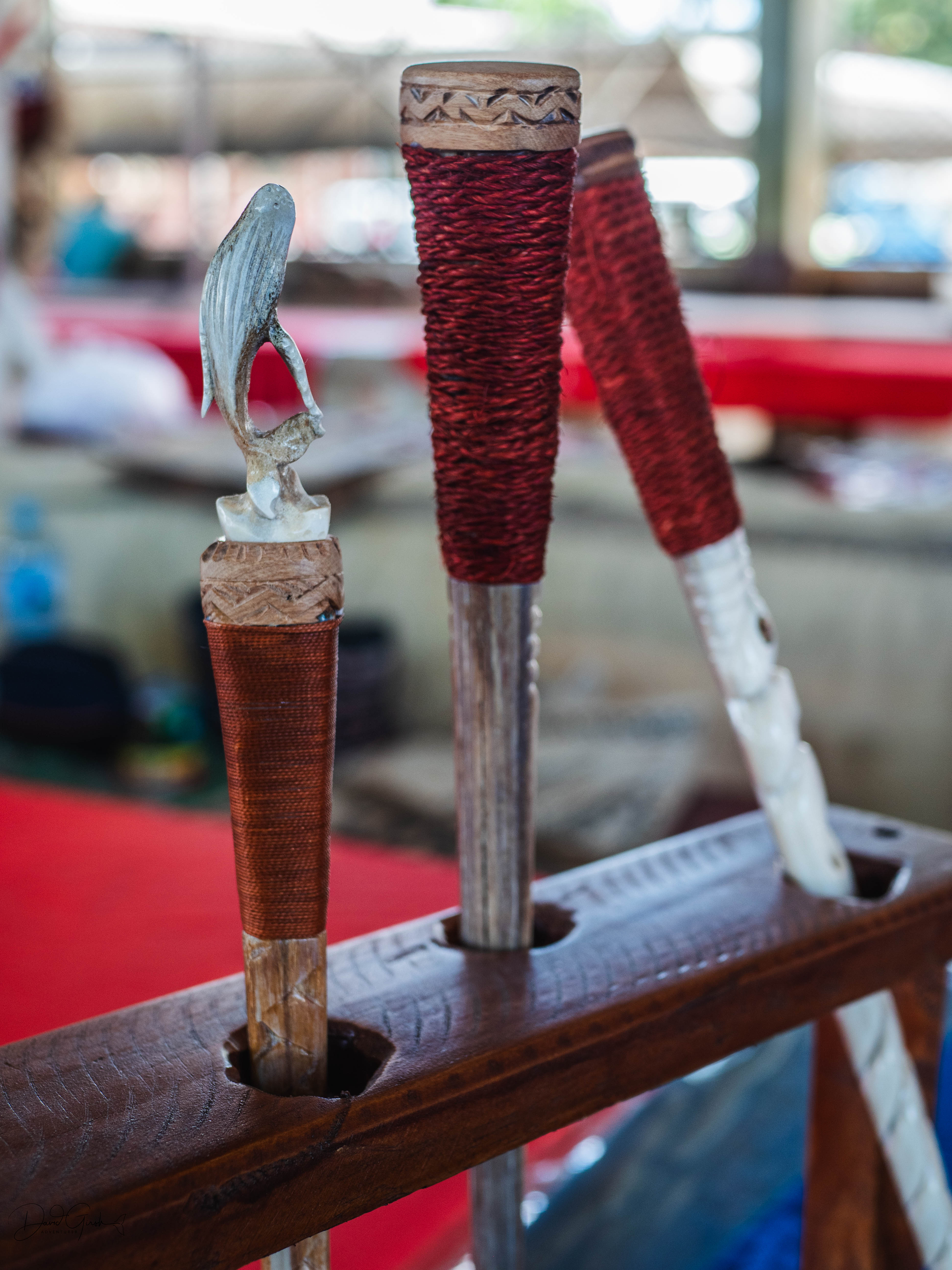 Carved war clubs with red cord wrapping and bone handles in a wooden rack