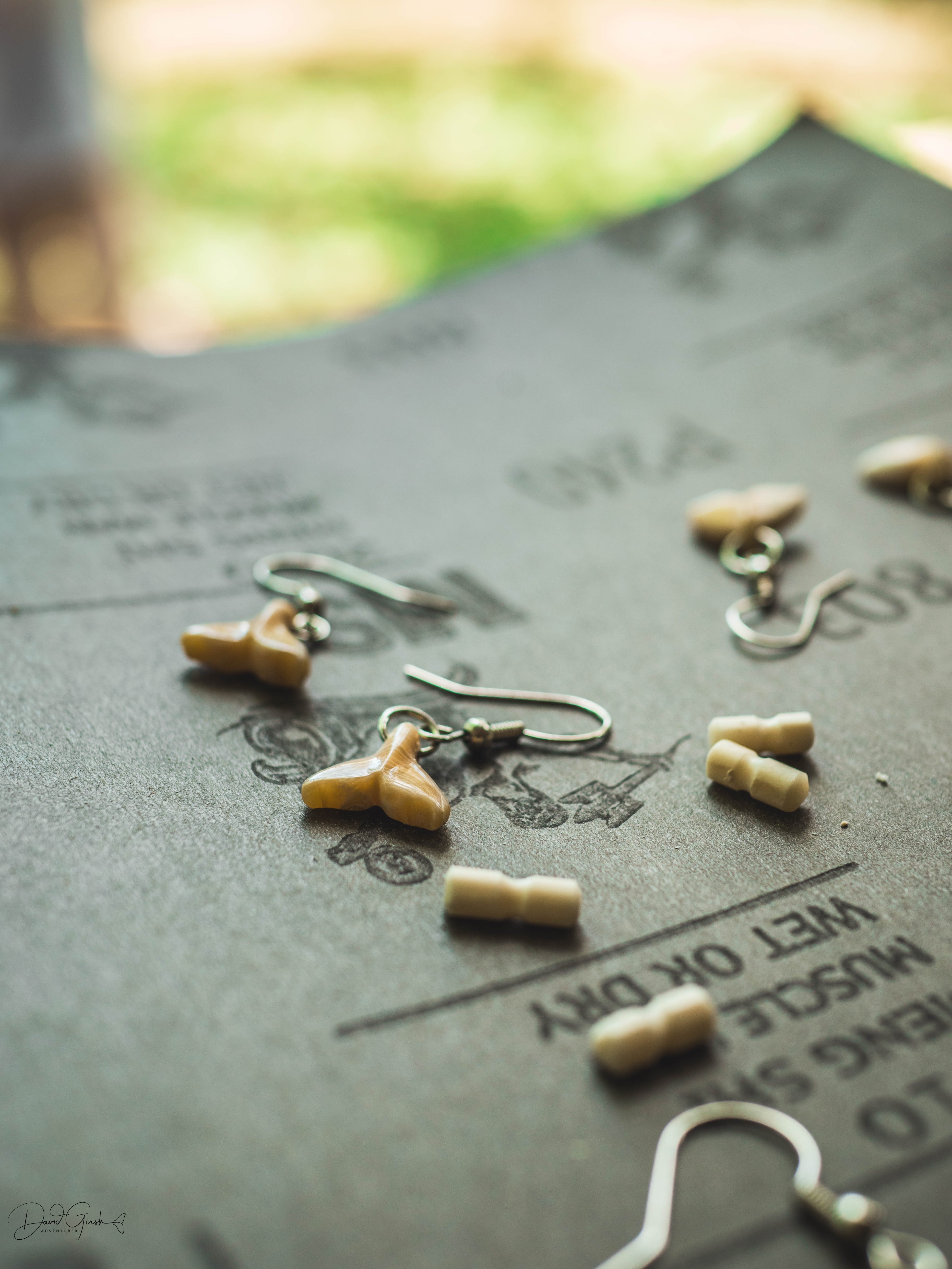 Tiny whale tail earrings on sandpaper, small enough to sit on a fingertip
