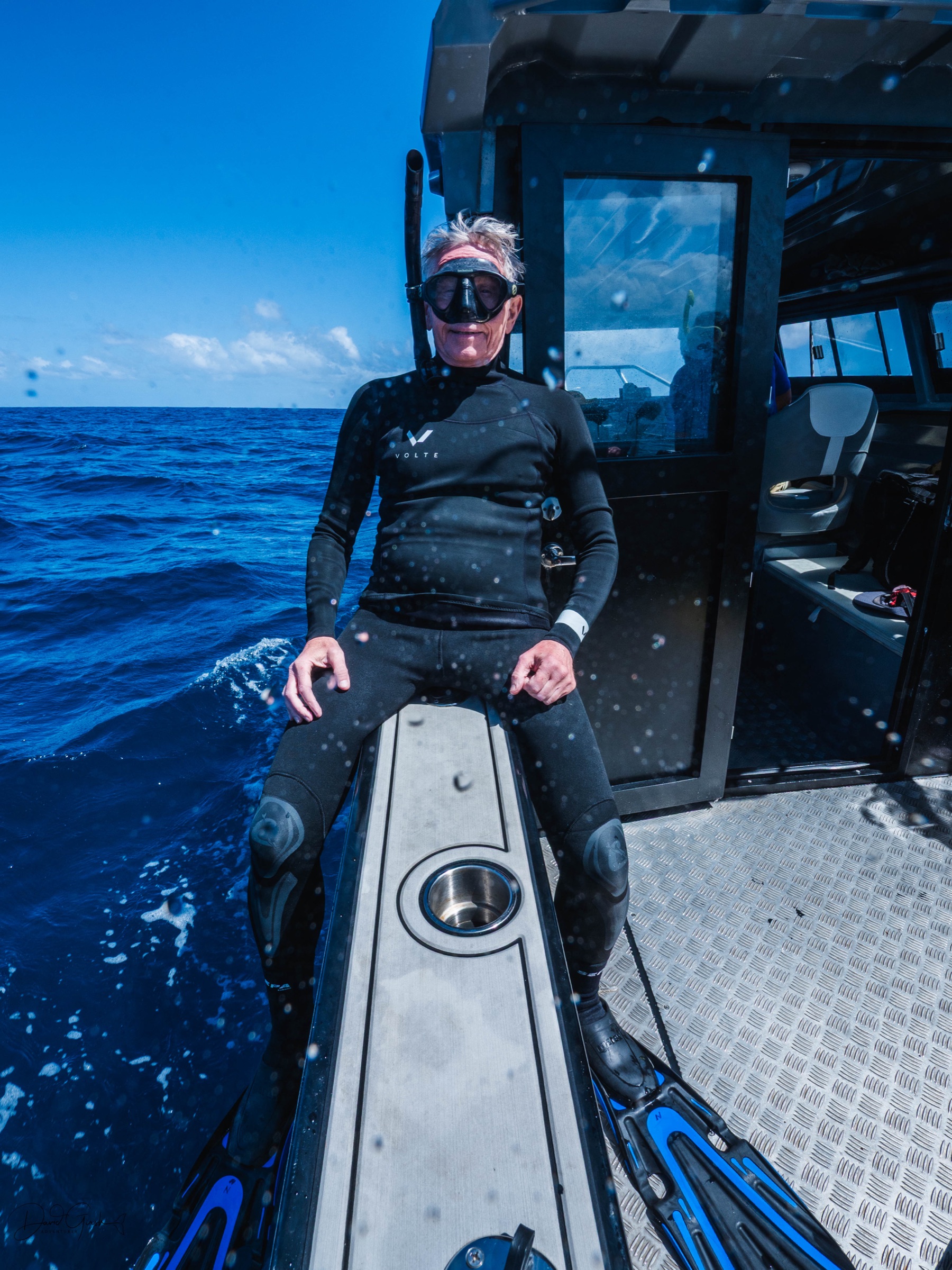 A guest in a wetsuit and mask sitting on the gunwale of the boat in open water, ready to go in