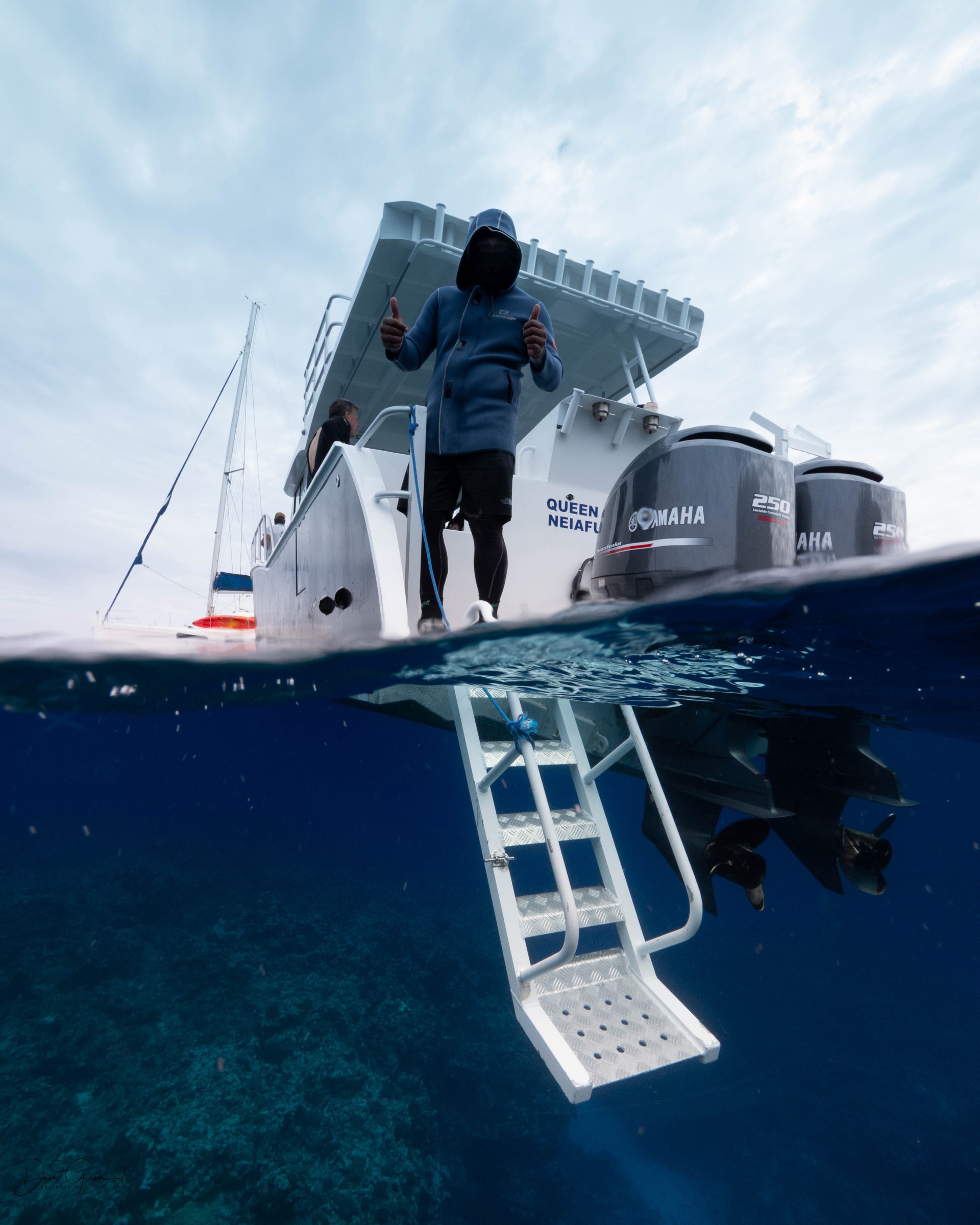 Split level view of the expedition boat at rest, crew on the back deck and the swim ladder running down into clear water over the reef