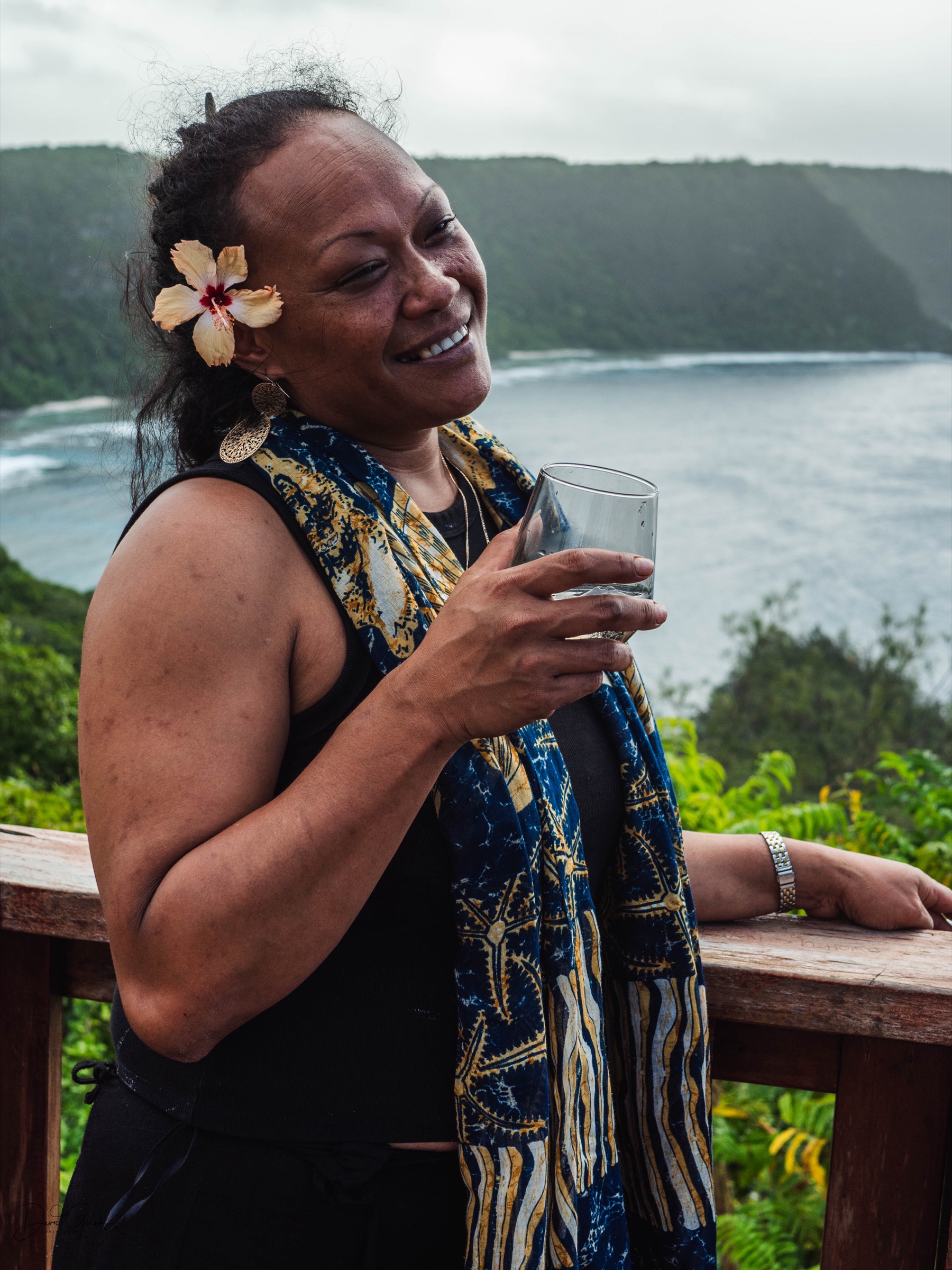 A Tongan woman with a flower in her hair smiling during a village gathering
