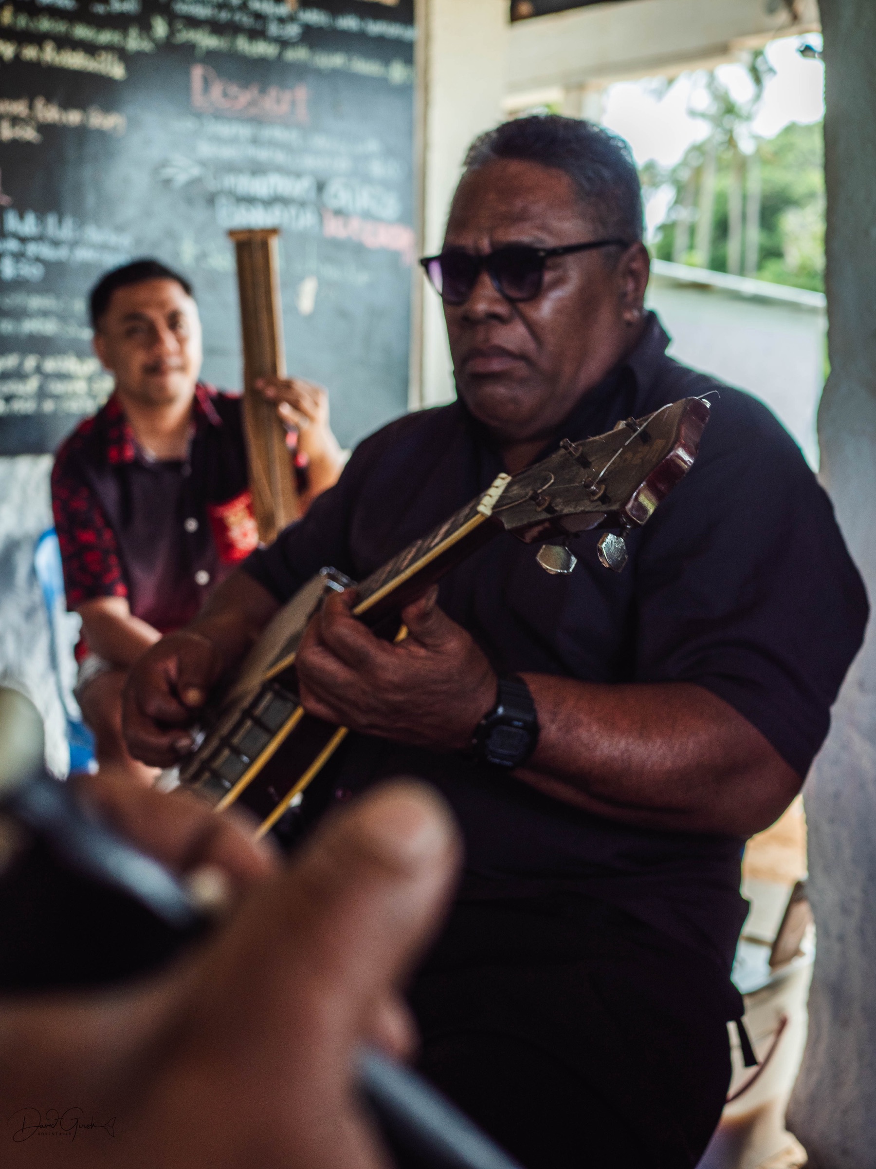 Local Tongan musicians playing stringed instruments together during a village gathering
